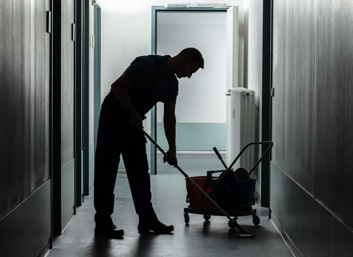 Silhouette of a janitor cleaning a dimly lit hallway with a mop and bucket cart suggesting urgent need to leave stories.