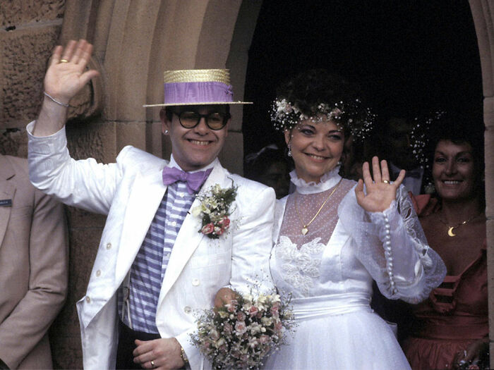 Pareja de celebridades en boda vintage sonriendo y saludando con trajes clásicos, símbolo de matrimonios de celebridades olvidados.