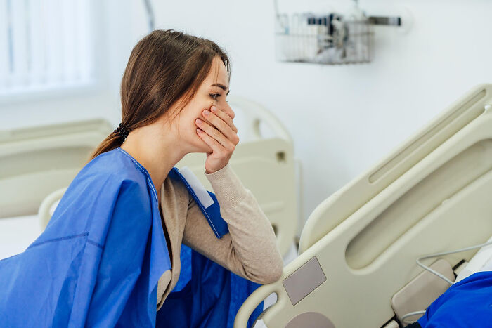 Woman in hospital gown covering her mouth, reacting to scary ghost stories during hospital work in a patient room.