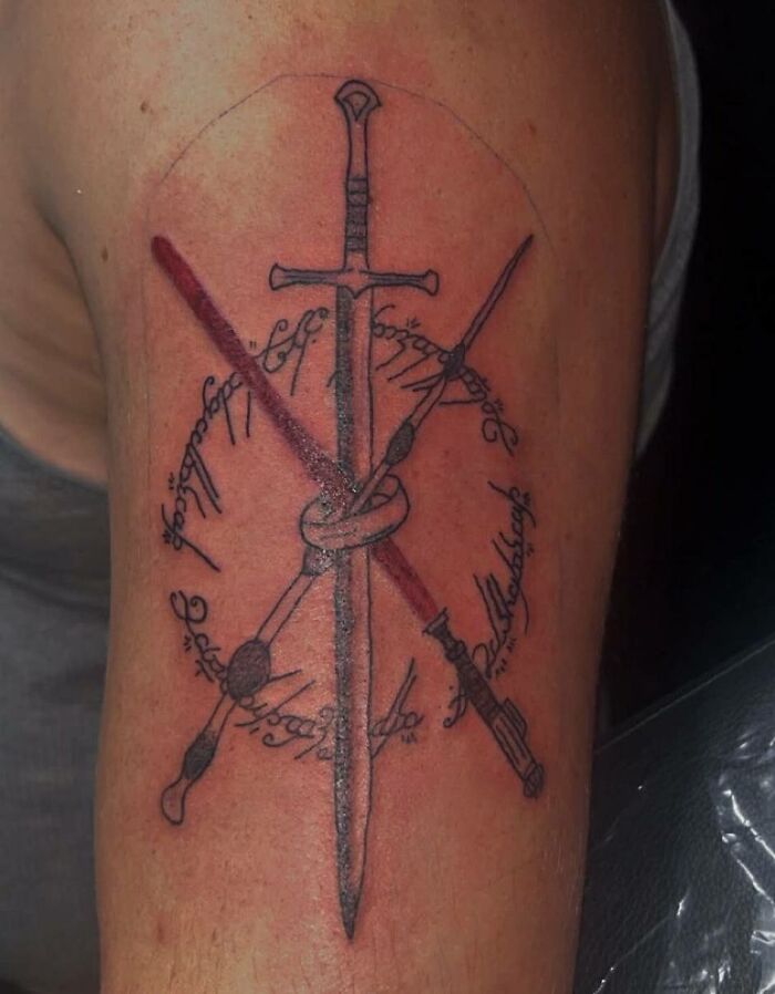 Tattoo of a sword and crossed lightsabers with circular script on upper arm, showcasing unique tattoo designs on skin.