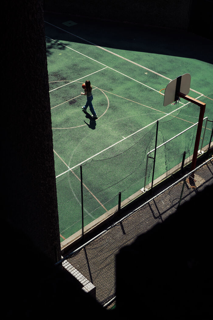 Young woman holding basketball alone on an empty court, showcasing stunning street photography capturing life's unexpected moments.