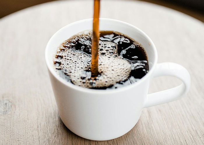 Pouring coffee into a white cup on a wooden table, illustrating simple life hacks people discovered accidentally.