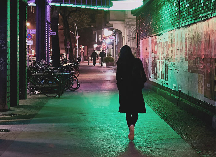 Person walking alone at night on a dimly lit urban sidewalk, evoking wild we need to leave right now stories.