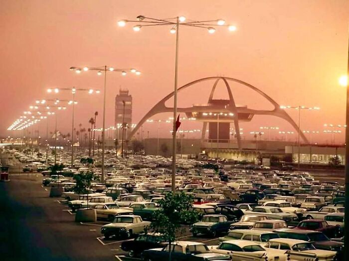 Vast parking lot filled with cars at sunset near a futuristic terminal, capturing a beautiful yet unnerving liminal space.