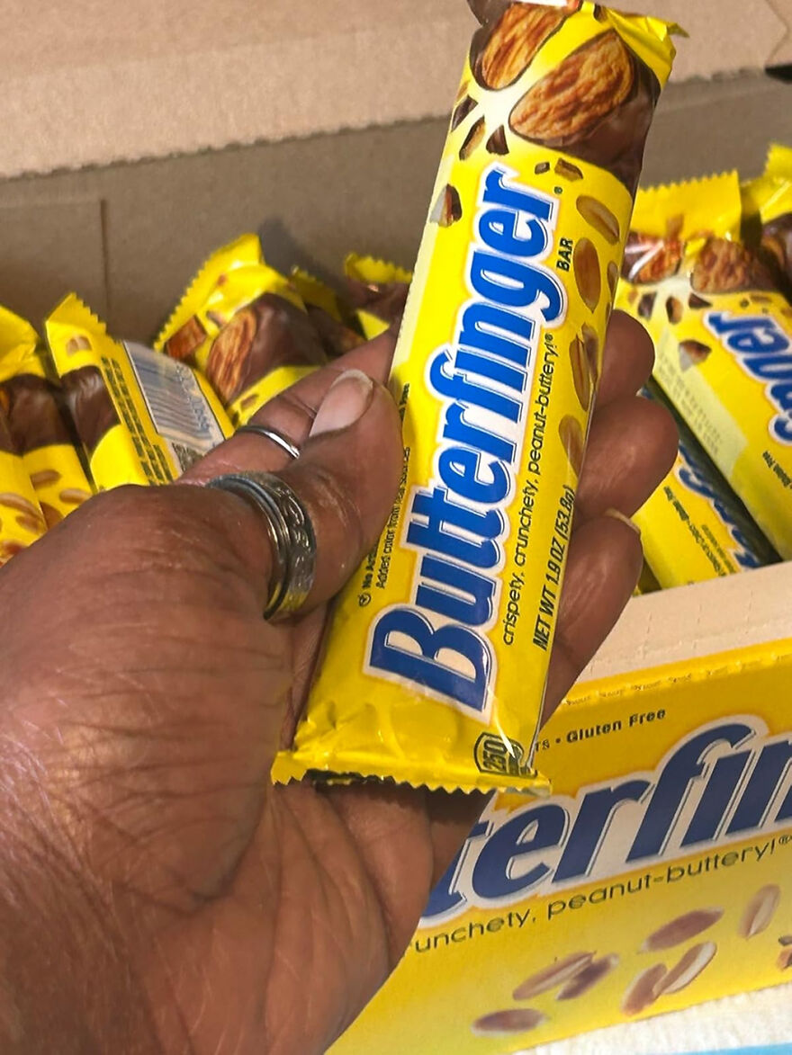 Hand holding a Butterfinger candy bar with multiple Butterfinger bars in a box, popular Halloween candy concept.