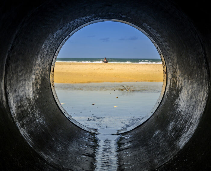 View of beach and ocean through large pipe opening, illustrating hidden dangers like terrifying medical conditions without symptoms.