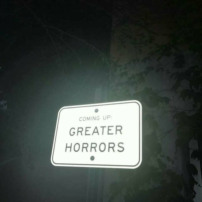 Road sign reading Greater Horrors at night surrounded by darkness, a confusing image where things only get weirder the longer you look.
