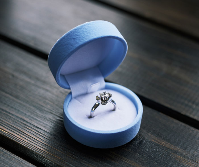 Engagement ring in an open blue velvet box on a wooden surface, symbolizing man proposes after breakup.