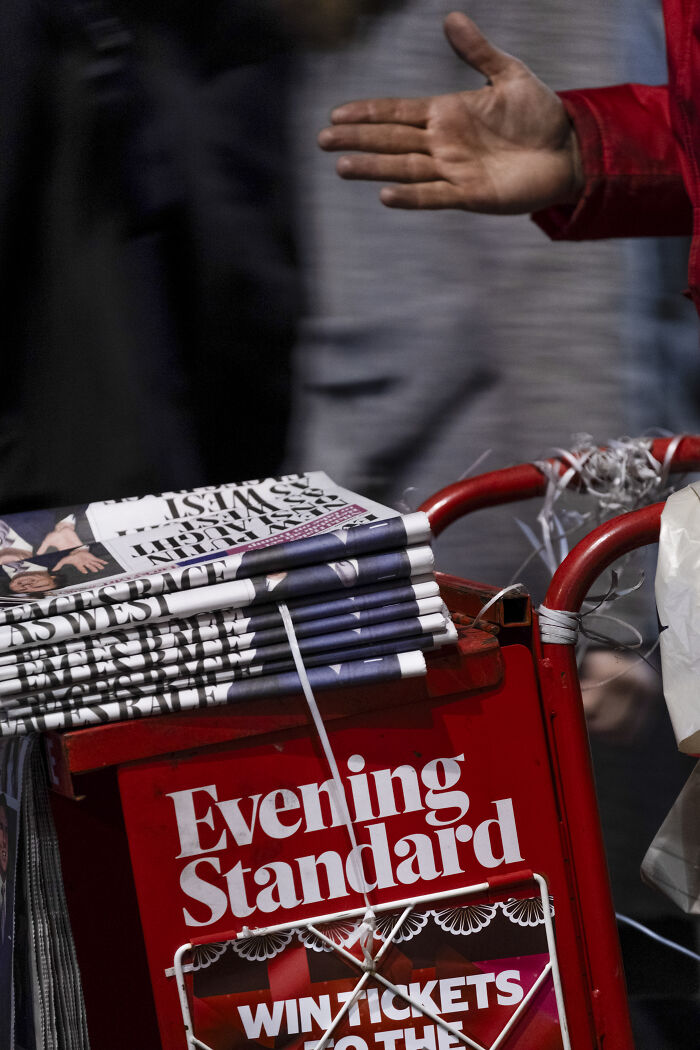 Stack of newspapers in a street photography shot capturing life’s unexpected moments with a hand reaching out nearby.