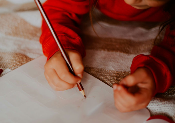 Child in red sweater holding pencil and drawing on paper, illustrating daycare workers hearing unexpected family secrets.