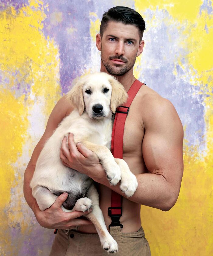 Muscular firefighter holding an adorable golden retriever puppy against a colorful yellow and purple textured background.