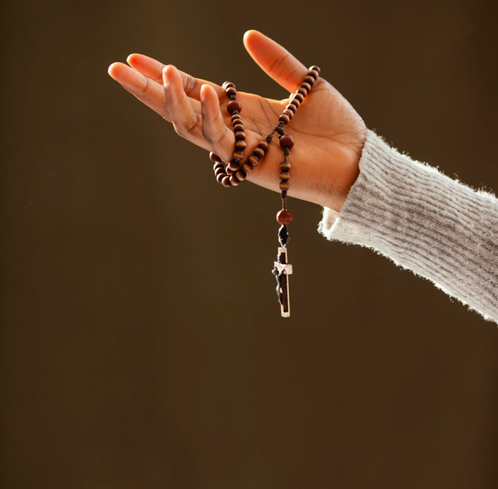 Hand holding wooden rosary beads with crucifix, symbolizing reflection on worst employees bosses have shared.