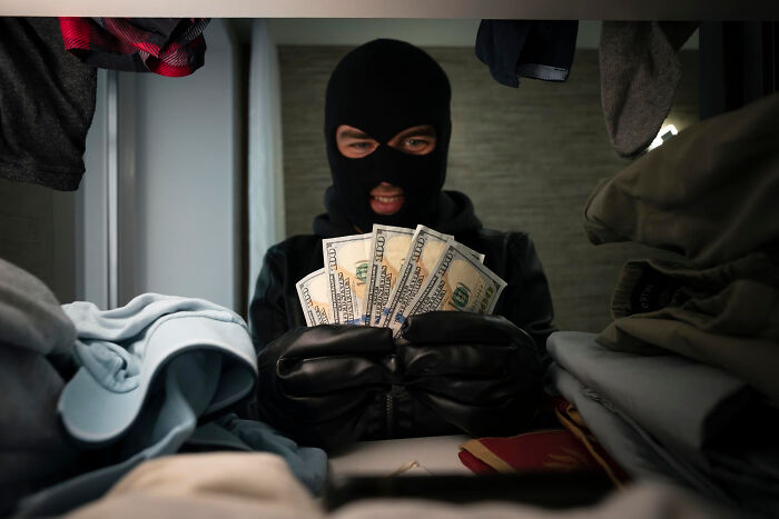 Person wearing mask and gloves holding several 100 dollar bills inside a cluttered closet, highlighting unfiltered dementia moments.