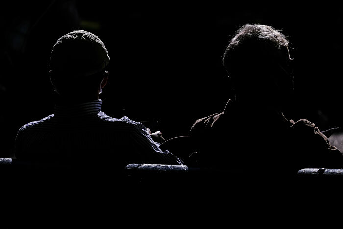 Two people sitting side by side in low light, captured in stunning street photography highlighting life’s unexpected moments.