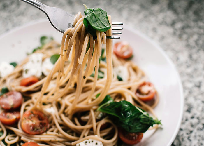 Fork twirling spaghetti with cherry tomatoes and spinach, demonstrating life hacks people discovered accidentally.