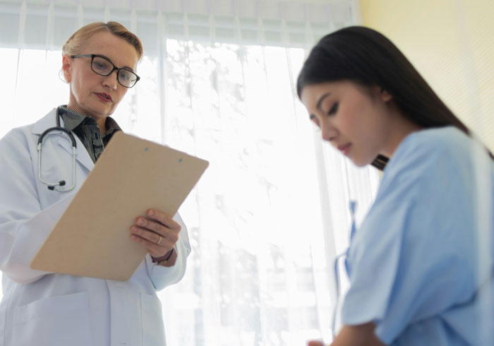 Female plastic surgeon reviewing notes while consulting a young patient about unnecessary surgeries in a bright medical office.