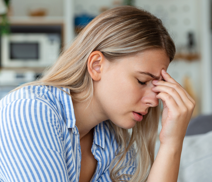 Young woman in a striped shirt holding her forehead, showing signs of illness and fever in a home setting.