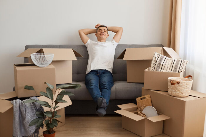 Man relaxing on couch surrounded by open moving boxes, illustrating zip-line your boxes out moving advice concept.