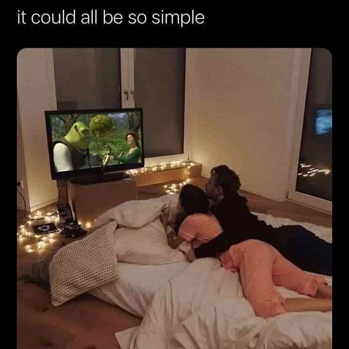 Couple lying on bed watching Shrek on TV, illustrating relatable memes about relationships in a cozy room with string lights.