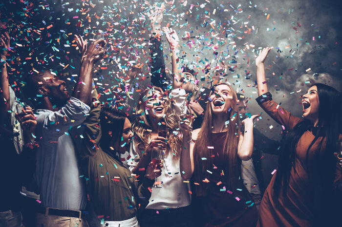 A group of friends celebrating with confetti, smiling and enjoying a lively party atmosphere in a dark room.