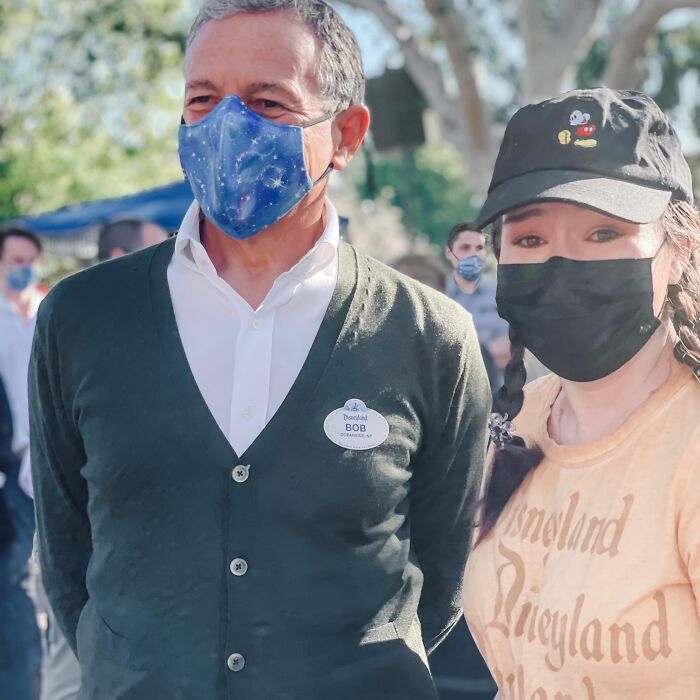 Man wearing a Disneyland cast member badge and blue face mask standing next to a woman in a Mickey cap and black mask outdoors.