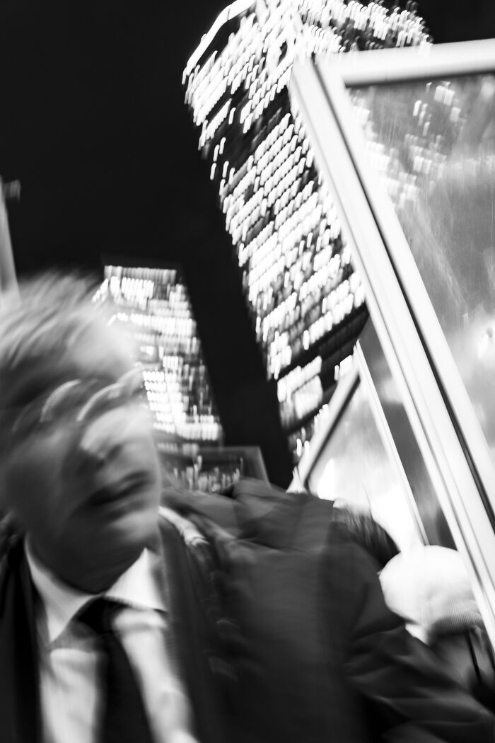 Blurred street photography shot of a man in a suit with city lights capturing life’s unexpected moments at night.