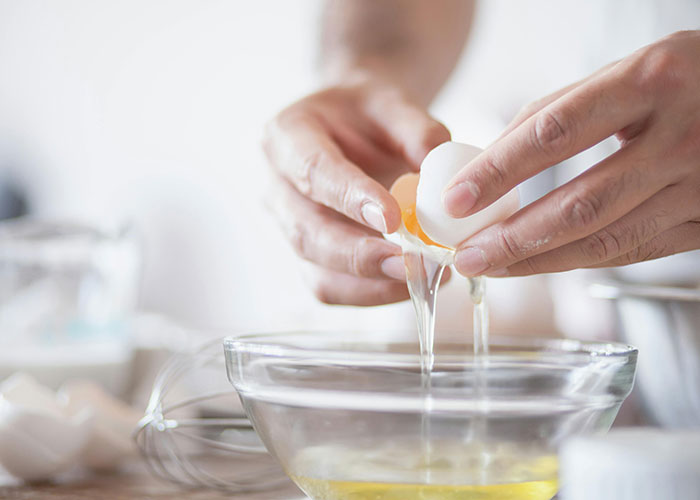 Person cracking an egg into a glass bowl demonstrating accidental life hacks used daily in the kitchen.