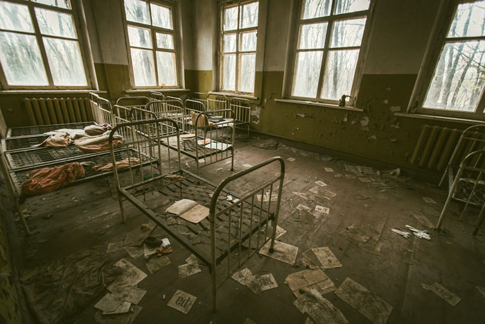 Abandoned room with rusty metal beds and debris on the floor, evoking a scene linked to worst crimes in hometowns.