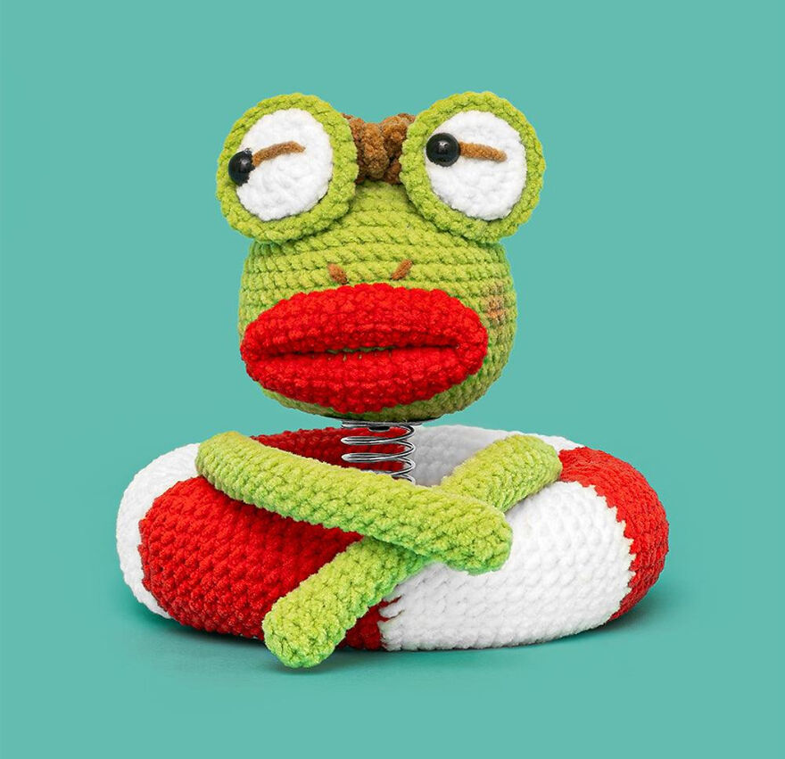 Crochet animal frog with big eyes and red lips sitting on a red and white float ring with crossed arms