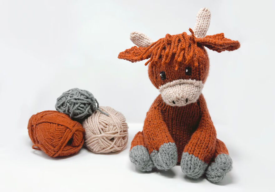 Crochet animal resembling a brown and gray cow sitting next to yarn balls, showcasing crochet animals with personality.