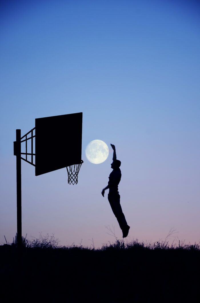 Silhouette of a basketball player jumping near a hoop with the moon in the background in an award-winning photo.