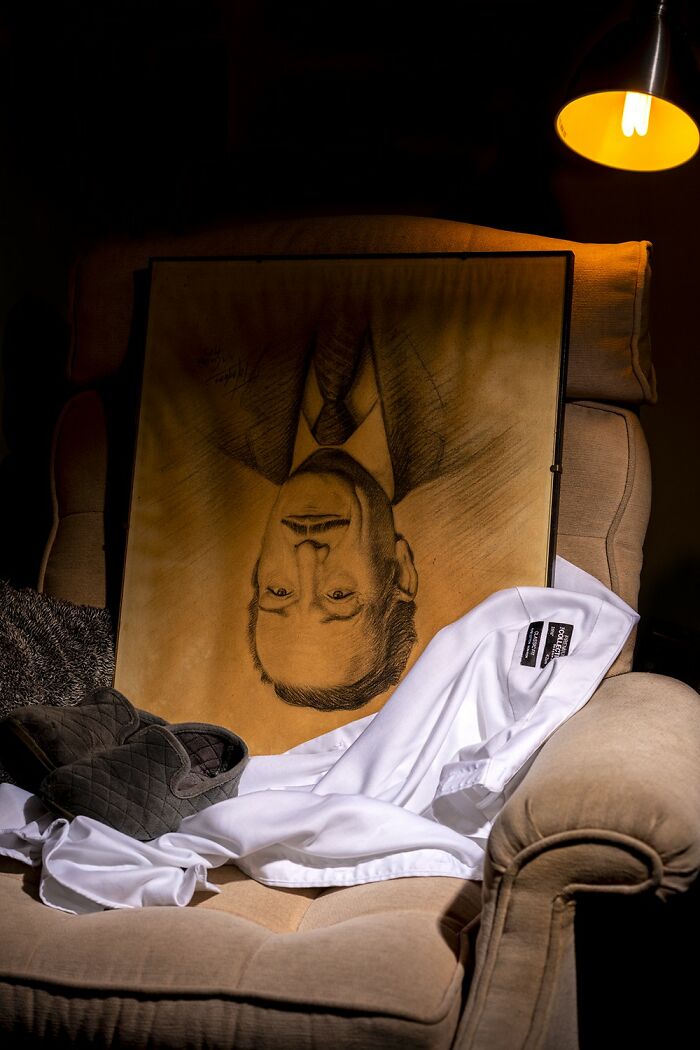 Award-winning photo of a vintage portrait on a chair with slippers and a white shirt illuminated by a warm lamp light.