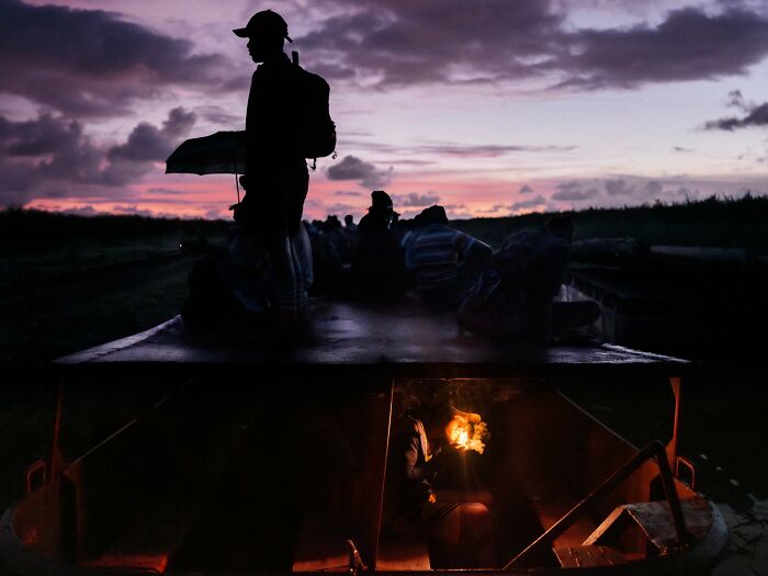 Silhouetted people on a boat at sunset and a warm fire inside, featured in award-winning photography contest.
