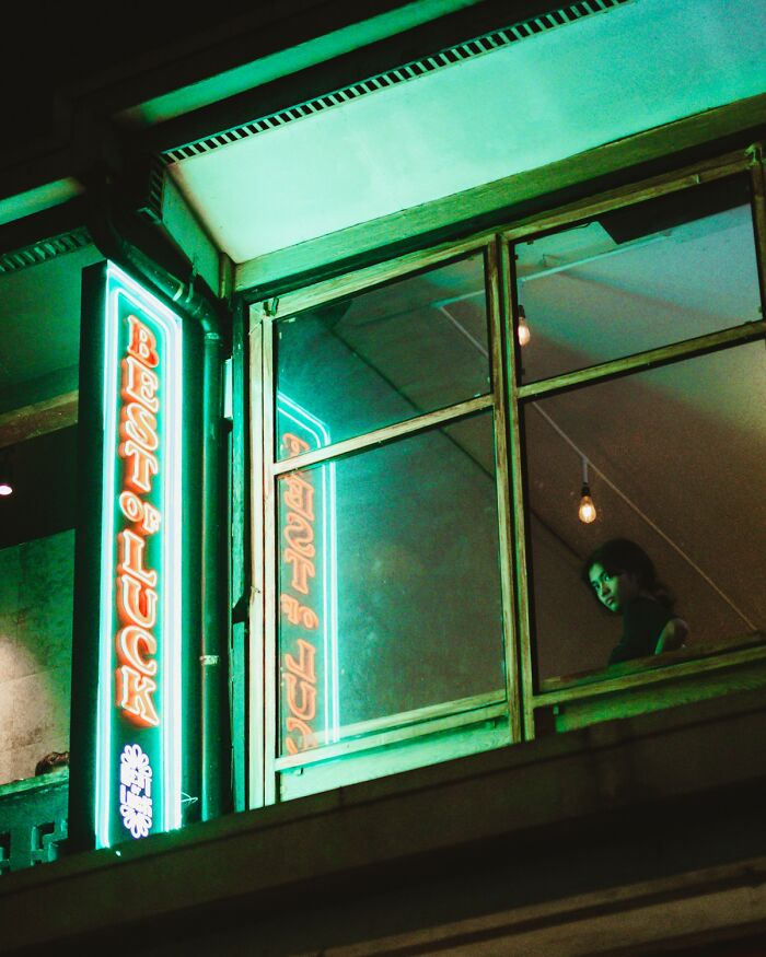 Neon sign reading Best of Luck with a person seen through a window in an award-winning photo from Photographer of the Year contest