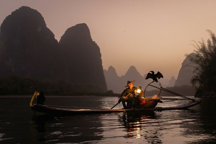 Fisherman on a boat at dusk with birds, captured in one of the award-winning photos from the 2025 Photographer Of The Year contest.