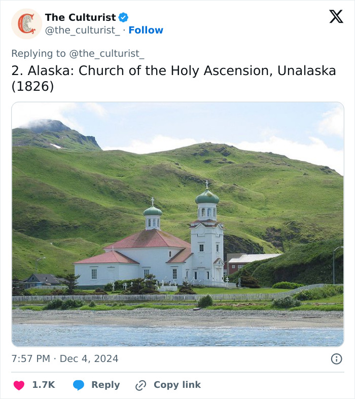 Church of the Holy Ascension in Alaska, a striking church surrounded by green hills near a calm shoreline.