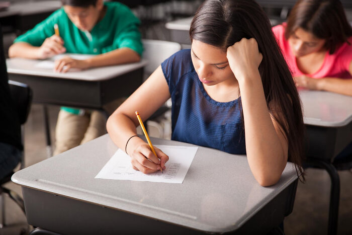 Teen girl focused on test paper while seated in classroom, illustrating awkward moments of misreading social cues.