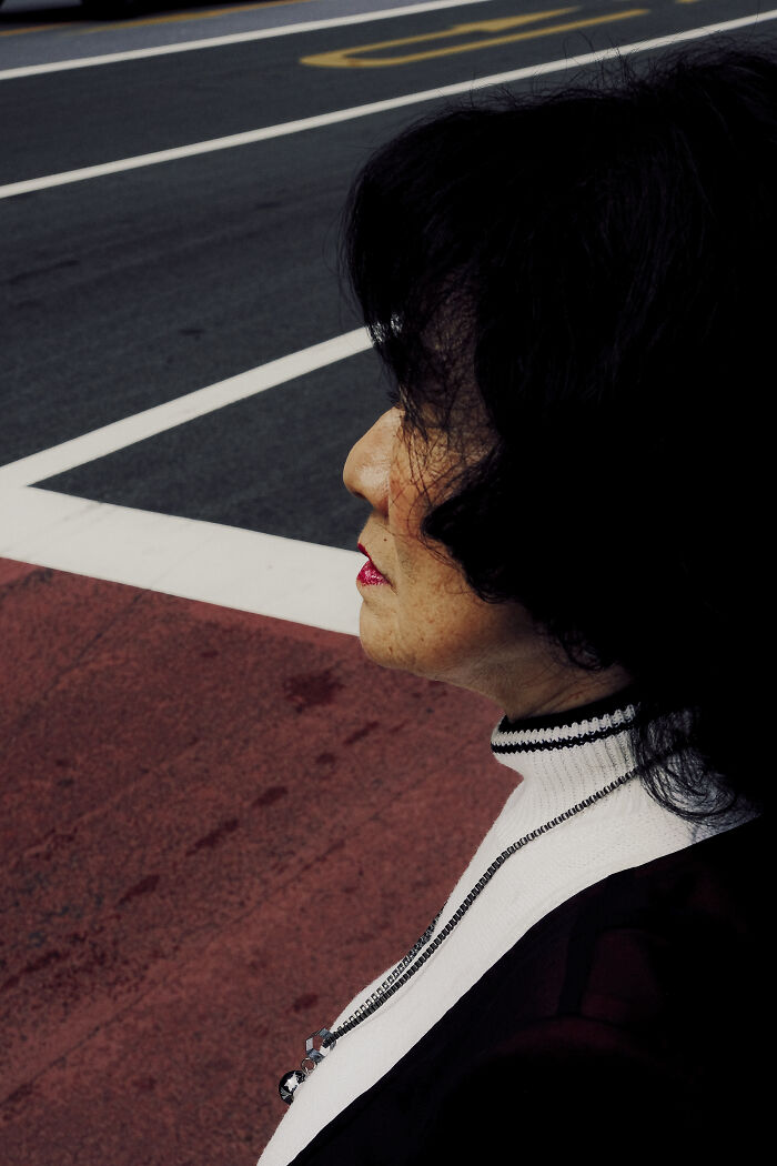 Woman with black hair and red lipstick standing by crosswalk, captured in stunning street photography shot on urban sidewalk.