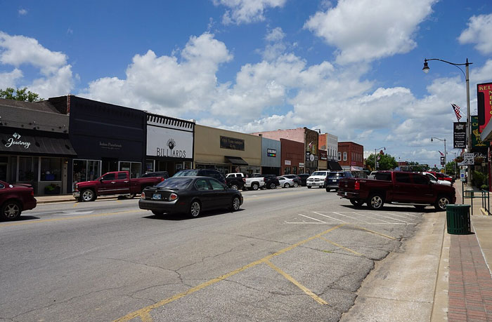 Small Midwestern main street with cars and shops under blue sky, evoking worst places travel tales