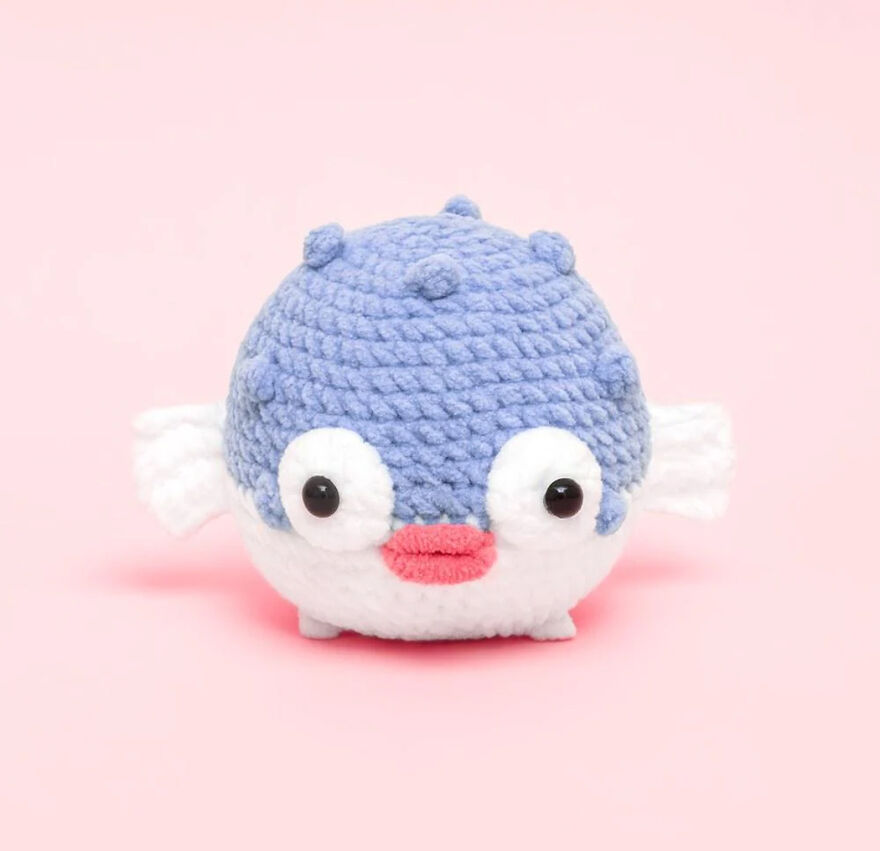 Crochet animal pufferfish with big eyes and textured blue and white yarn body on a pink background.