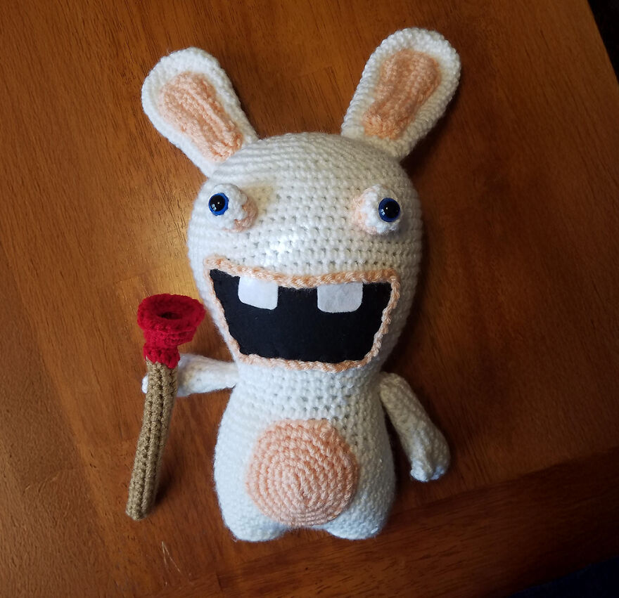 Crochet animal with large eyes and teeth holding a red flower, showcasing personality in handmade crochet art.