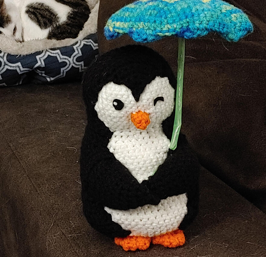 Crochet penguin animal holding a blue umbrella with a wink, showcasing crochet animals with personality.