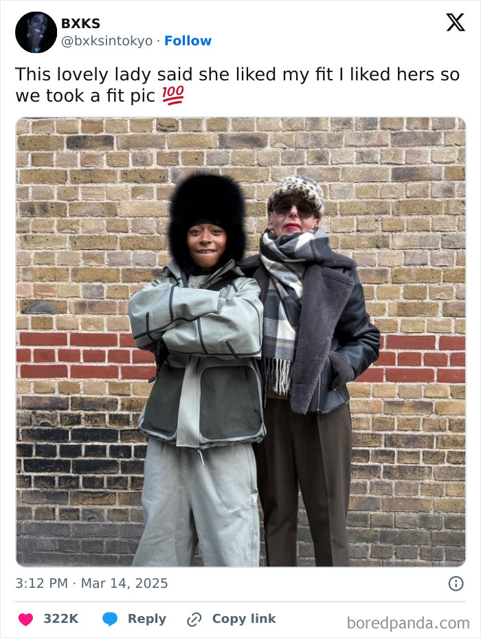 Two strangers pose together against a brick wall, showcasing their outfits and spreading faith in humanity restored.