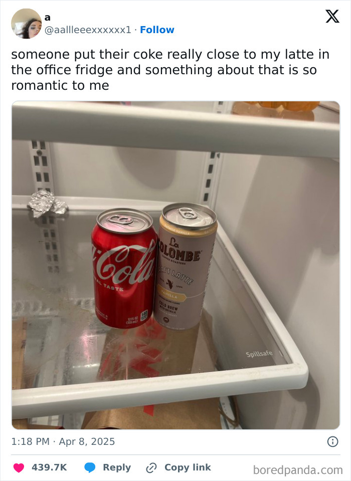 Two beverage cans, Coke and La Colombe latte, placed closely together inside an office fridge, highlighting funny tweets shared online.