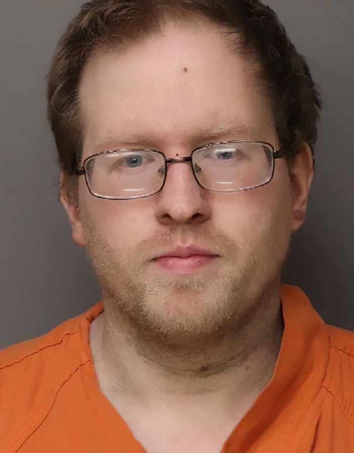 Man wearing glasses and an orange shirt, related to sister&rsquo;s emotional reaction after missing brother found alive news.