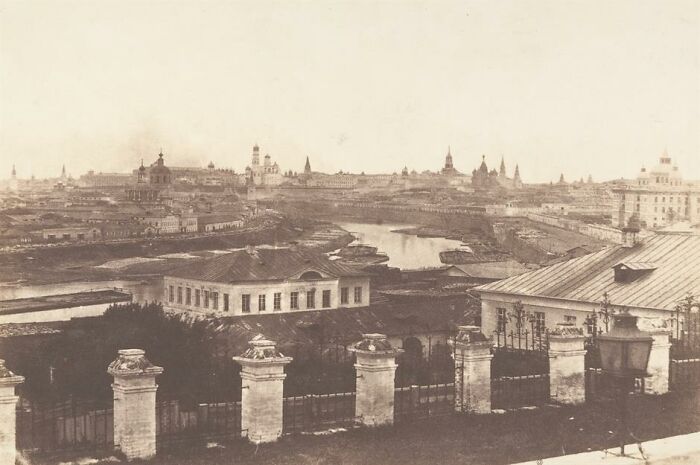 Sepia-toned photo showing an old view of a world capital with historic buildings and a river before modern times.