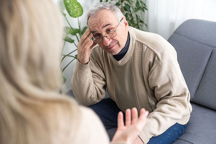 Older man in beige sweater talking with woman, illustrating man siding with daughter's cheating ex during divorce.
