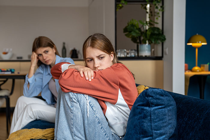 Woman looking upset on couch while her petty sister sits behind her, creating conflict instead of seeking therapy. Woman looking upset on couch while her petty sister sits behind her, creating conflict instead of seeking therapy.