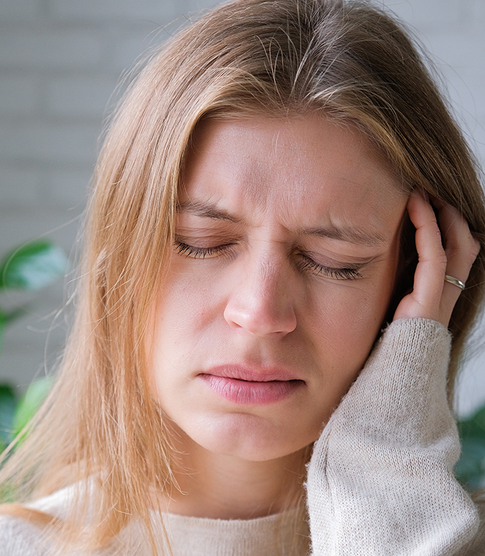 Young woman with eyes closed and hand on head looking distressed, illustrating service dog fraud confrontation emotions.
