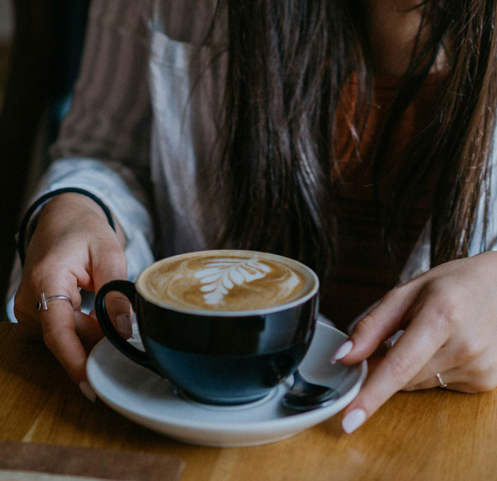Person holding a black coffee cup with latte art, illustrating the market has changed and company salary claims.